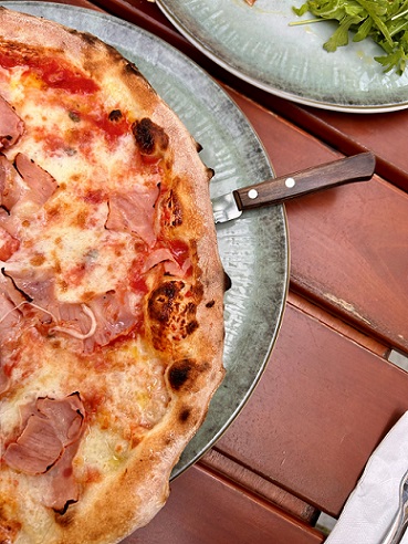 Teller mit halber Pizza mit Schinken, Holztisch