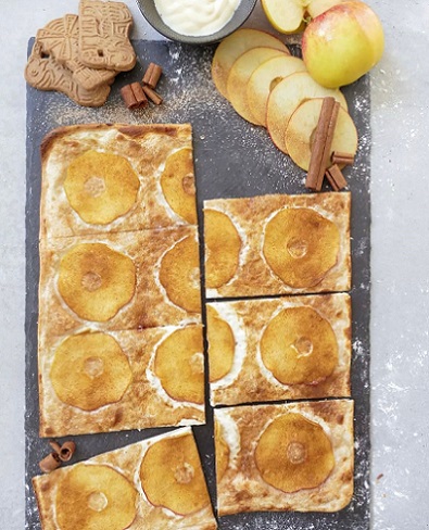 Flammkuchen mit Apfelscheiben und Zimt auf Schieferplatte dekoriert mit Spekulatius, Apfelscheiben und Zimtstangen