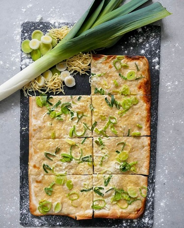 Flammkuchen belegt mit Lauchzwiebeln auf Schieferplatte dekoriert mit Geschnittenen und ungeschnittenen Lauch