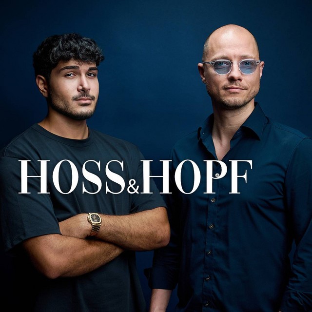 Hoss&Hopf dunkelblauer einfarbiger Hintergrund. 2 stehende Männer, einer leicht gedreht zum anderen mit verschränkten Armen und dunklem T-Shirt. Der andere im dunkelblauen Hemd und graublauer Sonnenbrille. In weißer Schrift steht: Hoss & Hopf"