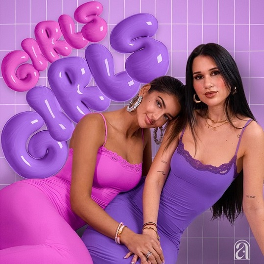 GirlsGirls Lila Hintergrund, links oben steht untereinander in einer Bubbleschrift in rosa und lila "Girls Girls". Im Vordergrund sitzen zwei junge Frauen aneinander gelehnt. Die linke hat ein Rosanes enges Kleid an und große silberne Ohrringe und lehnt sich an die Rechte. Die rechte Frau hat ein lilanes, enges Kleid an, dunkle lange, glatte Haare und stütz sich mit der linken Hand am Boden