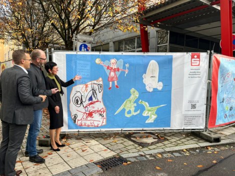 Drei Mitarbeiter der Sparkasse beim betrachten eines bunten Bauzaunbanners. 