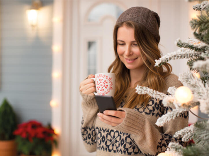 Frau mit Tasse und Handy in weihnachtlicher Stimmung