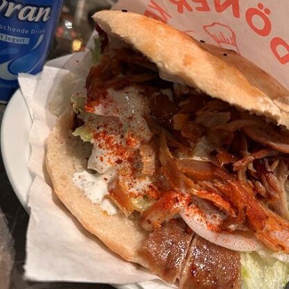 Döner in Papier auf Teller mit Serviette, daneben ein Ayran